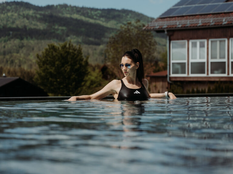Eine Frau mit Sonnenbrille entspannt bei Sommerwetter im Aussenpool des Hotel Tonihof im Bayerischen Wald.