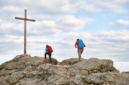 Zwei Personen wandern bei perfekten Wanderwetter zum Gipfelkreuz.