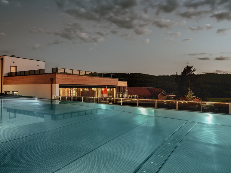 Ein stimmungsvoller Blick auf den einladenden Pool des Tonihof, vor der Kulisse des sanft beleuchteten Hotelgebäudes bei Nacht.