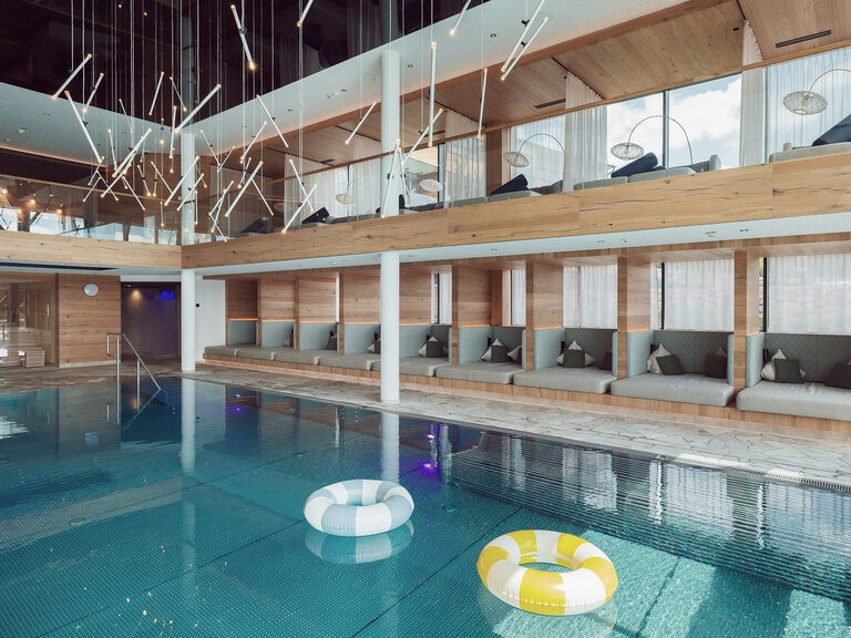 Der weitläufige Innenpool des Tonihofs, auf dessen Wasser bunte Schwimmreifen treiben, umrahmt von gemütlichen Liegen.