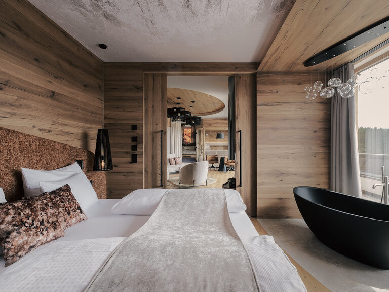 Ein einladendes Schlafzimmer in der Suit des Tonihof mit einem komfortablen Bett und Badewanne und einem großen Fenster, das einen wunderbaren Ausblick eröffnet.